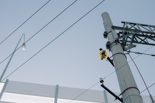Utility pole with electrical wires and equipment against a clear blue sky, showcasing urban infrastructure.